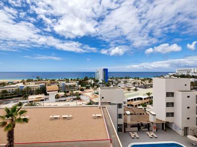 Vista di un hotel costiero con piscina, edifici e sfondo di mare e cielo azzurro