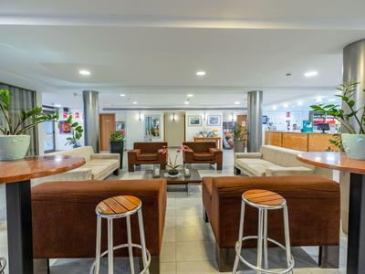 Moderne hotellobby met zitgedeeltes, barkrukken en planten in een lichte, ruime kamer.