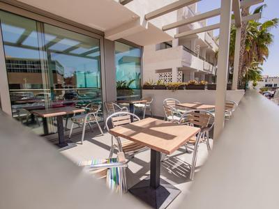 Area terrazza dell'hotel con tavoli, sedie e facciata in vetro sotto il sole.