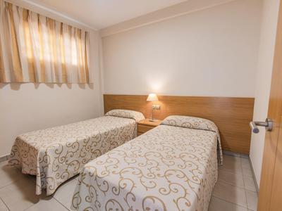 Una camera d'hotel semplice con due letti singoli e un comodino in mezzo.