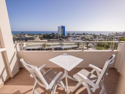 Balcone con tavolo e sedie bianchi con vista sul mare sotto un cielo azzurro limpido.