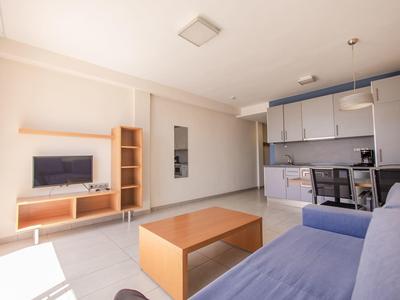 Soggiorno luminoso e moderno con divano, tavolino e angolo cottura integrato.