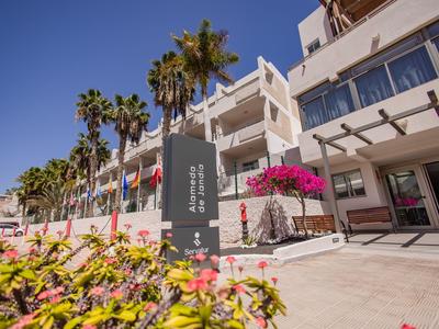 Buitenkant van een hotel met palmbomen en bloemen onder een heldere blauwe lucht.