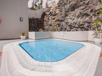 Vasca idromassaggio esterna moderna con acqua blu chiara accanto a parete rocciosa e muri bianchi.