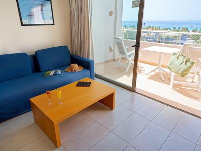 Woonkamer met blauwe bank, houten tafel en balkon met zeezicht