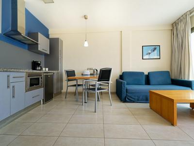 Moderne woonruimte met blauwe bank, houten tafel en kitchenette in een lichte kamer.