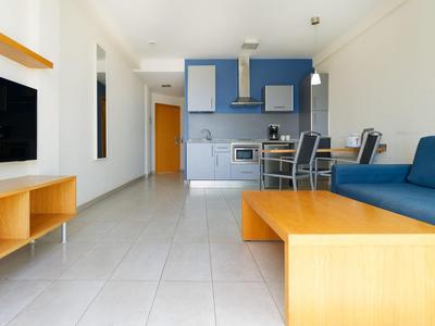 Moderner Wohnbereich mit blauer Couch, Holztisch und integrierter Küche in hellem Raum.