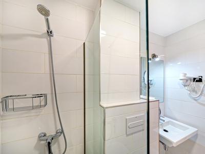 Modernes Badezimmer mit Walk-in-Dusche, Waschbecken und WC in weißen Fliesen.