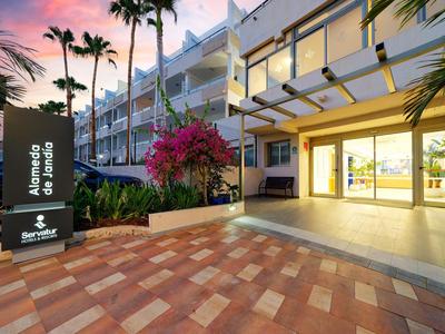 Moderne hotelentree met palmbomen en kleurrijke zonsondergang op de achtergrond.