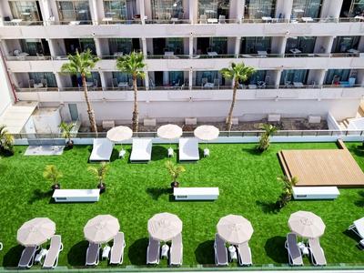 Uitzicht op een tuin met tafels, stoelen en ligstoelen voor een hotelgebouw.