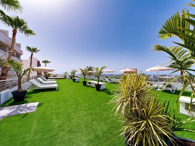 Groen grasveld met ligstoelen en parasols naast een hotel, bewolkte lucht.