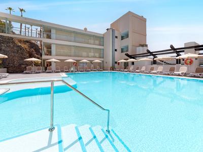 Groot hotelzwembad met blauw water, omringd door ligstoelen en parasols.