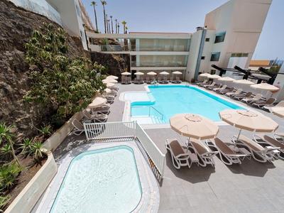 Moderne hotelterras met zwembad, hot tub, ligstoelen en tafels in een zonnige omgeving.