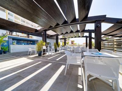 Moderne buitenruimte met witte stoelen en tafels onder houten pergola bij zonnig hotel.