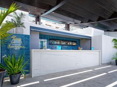 Moderne hotelbar met witte balie, blauwe accenten en planten onder een houten dak.
