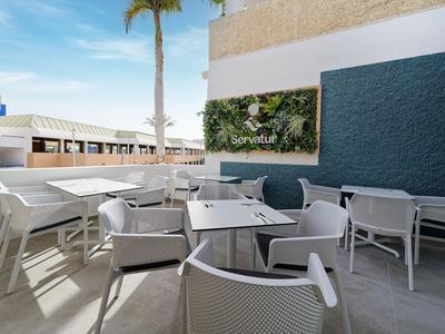 Moderne buitenterras met tafels en stoelen naast een verticale tuinmuur voor gasten.
