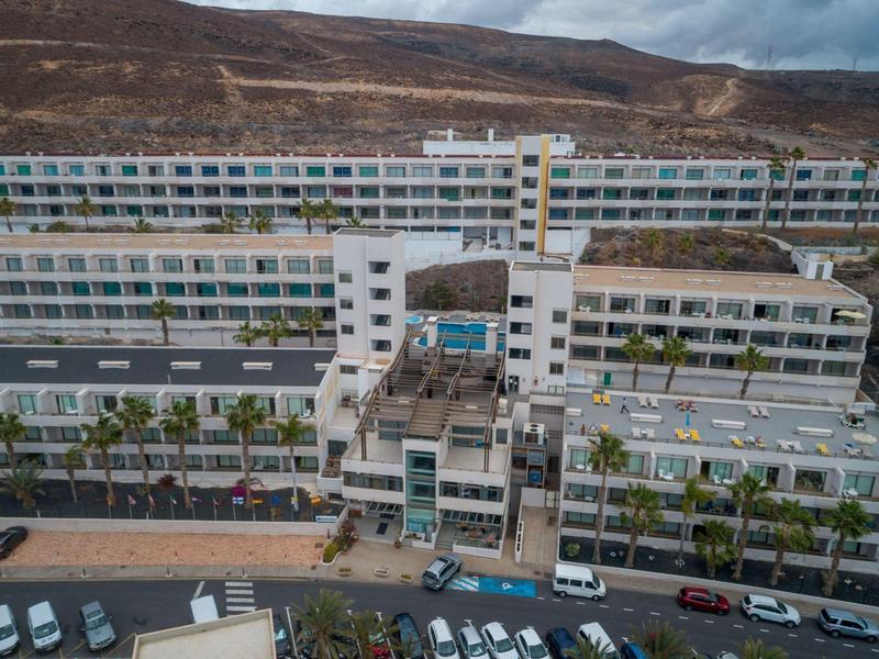 Grande edificio alberghiero a più piani con parcheggi e montagne sullo sfondo