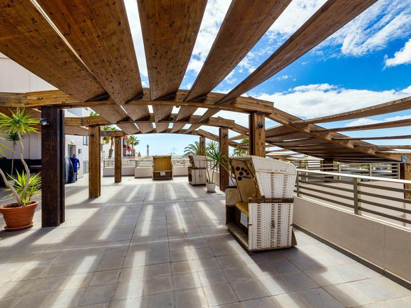 Area aperta sul tetto con travi in legno, posti a sedere e vista sul mare in una giornata di sole.