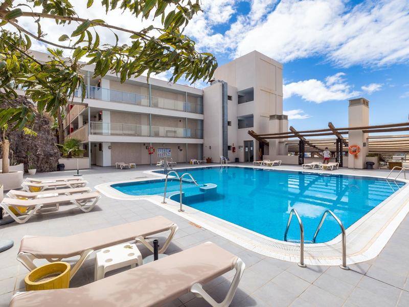 Area piscina esterna moderna con lettini e ombrelloni in un hotel in una giornata di sole.