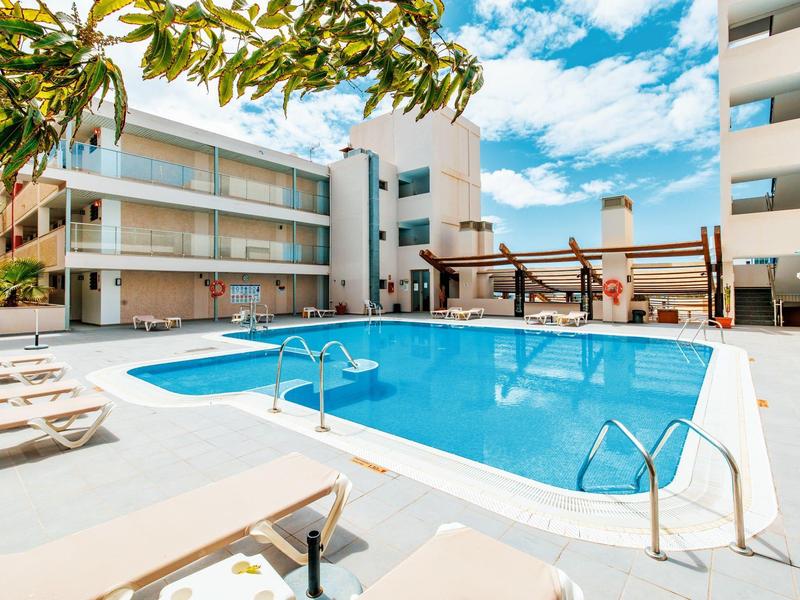 Area piscina esterna moderna con lettini tra alti edifici residenziali sotto un cielo limpido.