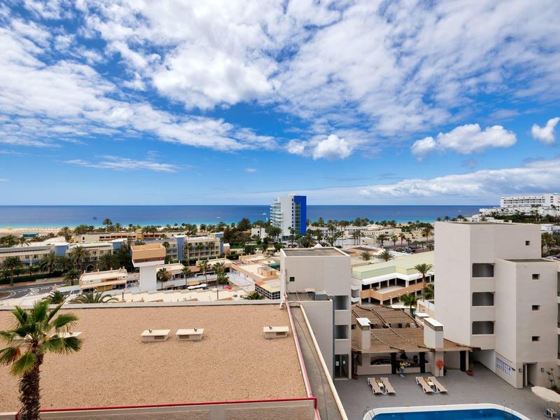 Vista di un hotel costiero con piscina, edifici e sfondo di mare e cielo azzurro