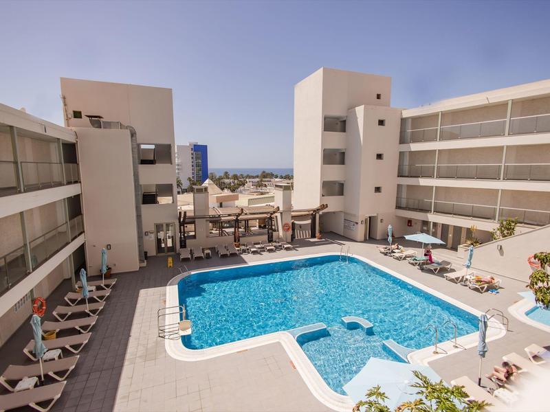 Piscina moderna dell'hotel con lettini tra edifici a più piani sotto un cielo sereno.