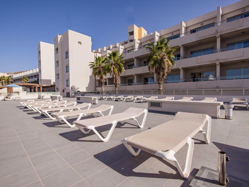 Lettini vuoti davanti a un edificio moderno di un hotel con palme sotto un cielo sereno.