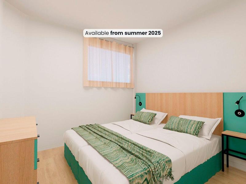 Camera d'hotel semplice e moderna con letto matrimoniale, biancheria verde e mobili in legno chiaro.