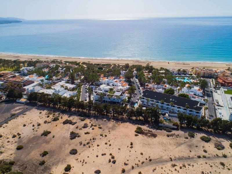 Veduta aerea di una località costiera con spiaggia, edifici e mare azzurro chiaro