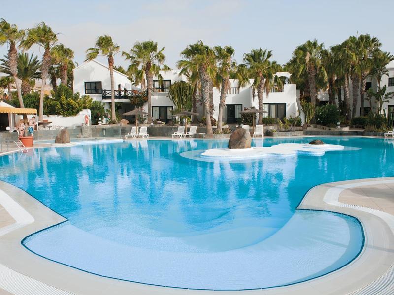 Piscina rotonda dell'hotel con acqua azzurra limpida, circondata da edifici bianchi e palme.