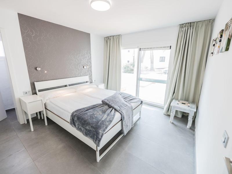 Camera d'hotel luminosa con letto matrimoniale, pareti e tende grigie, design moderno e minimalista.