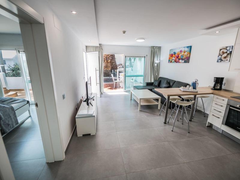 Zona living e pranzo moderna e aperta con cucina e accesso al balcone in toni chiari.