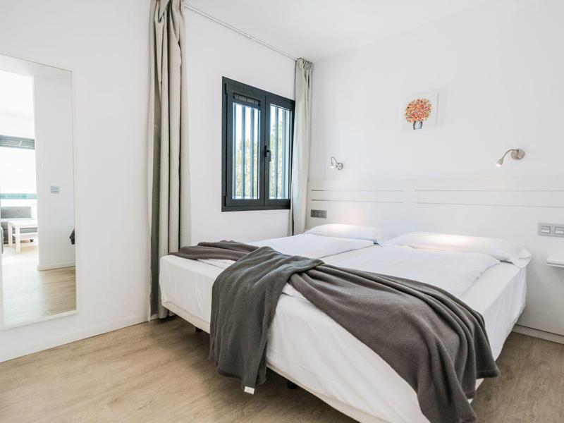 Camera d'hotel luminosa con letto matrimoniale, grande specchio e finestra con tende.