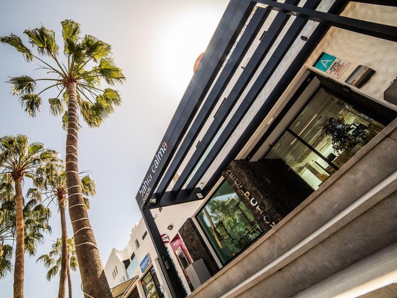 Vista di un'architettura alberghiera moderna con facciata in vetro e palme sotto un cielo soleggiato.