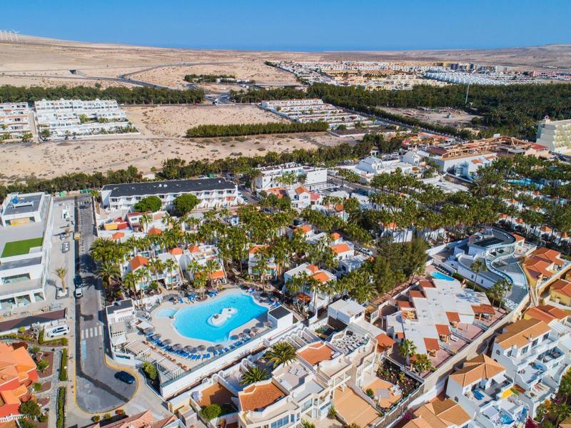 Vista aerea di un resort con piscina, circondato da edifici e paesaggio arido sullo sfondo.