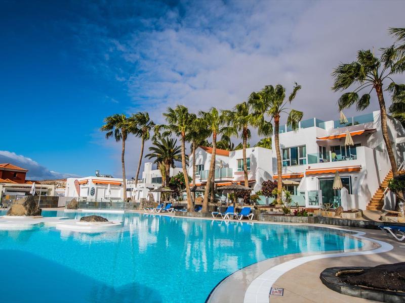 Piscina dell'hotel con palme, lettini e cielo azzurro in una giornata di sole.