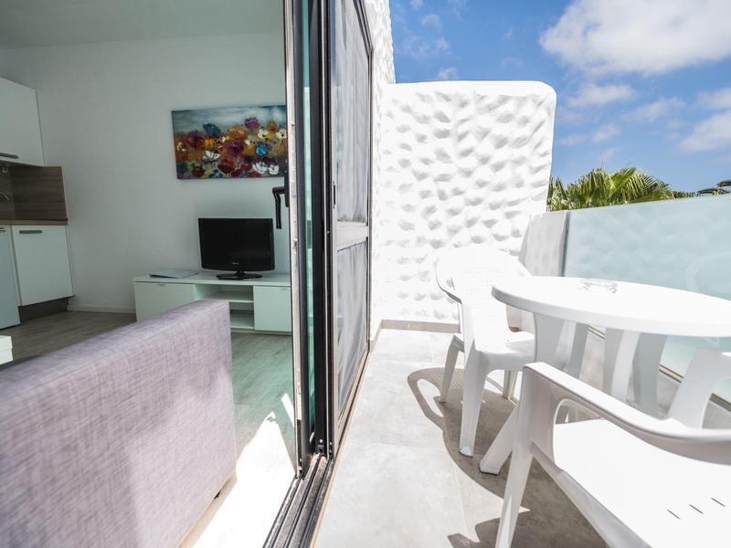 Appartamento moderno con balcone, area salotto bianca e vista sul cielo azzurro.