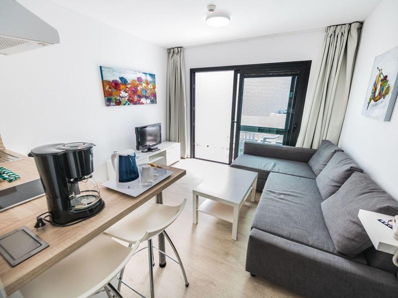 Soggiorno moderno con divano, tavolino e angolo cucina con macchina per il caffè.