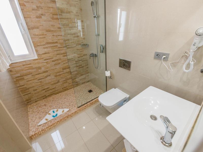 Bagno luminoso con doccia a filo pavimento, WC, lavabo e asciugacapelli.