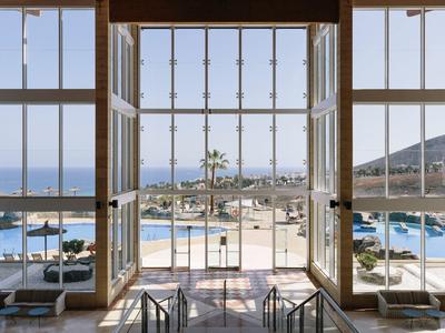 Open windows overlooking a sunny beach with chairs and umbrellas by the sea.