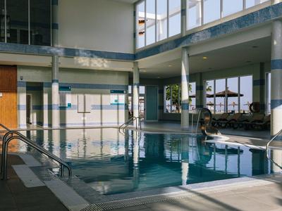 Indoor hotel pool with large windows letting in natural light and poolside seating.