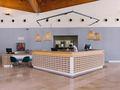 Modern hotel reception with a wooden ceiling, grey walls, and pendant lights over the desk.
