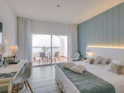 Modern hotel room with king bed, desk, and balcony with outdoor seating.