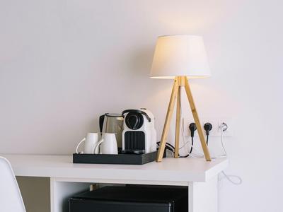 A desk lamp with tripods and a coffee maker with cups on a white desk.