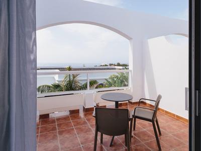 Balcony with two chairs and a small table overlooking the sea and palm trees.