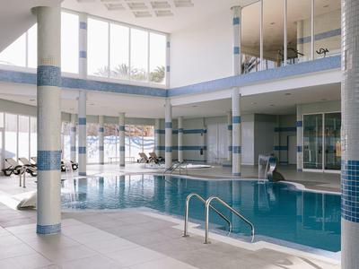 Indoor hotel swimming pool with blue tiles and glass windows letting in natural light.