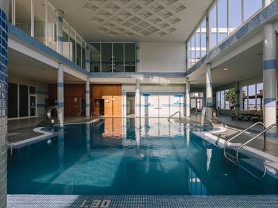 Indoor swimming pool with large windows and lounge chairs around it.