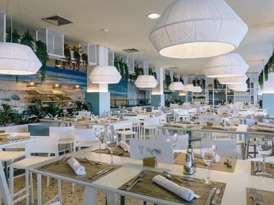 Spacious modern restaurant with white furniture, pendant lights, and table settings.