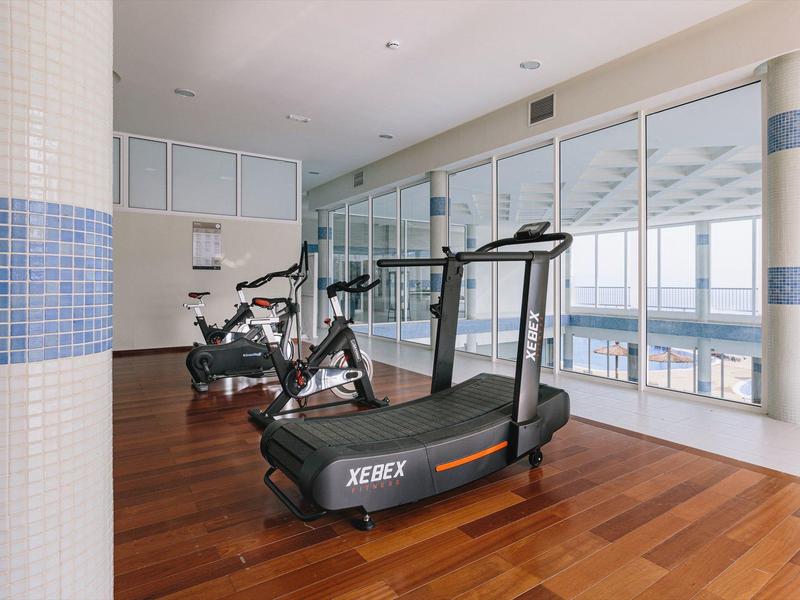 Modern gym with cardio equipment and large windows overlooking a scenic waterfront.