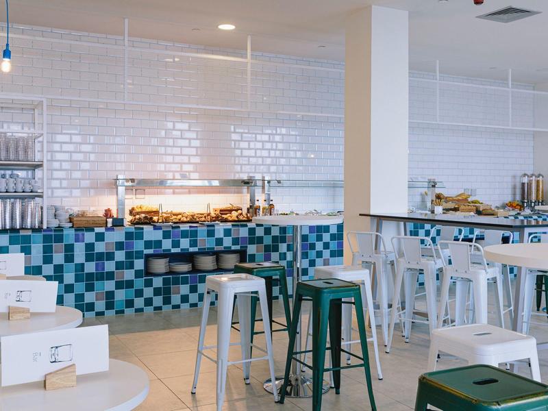 Modern breakfast area with bar stools, blue tiled counter, and grab-and-go boxed meals.